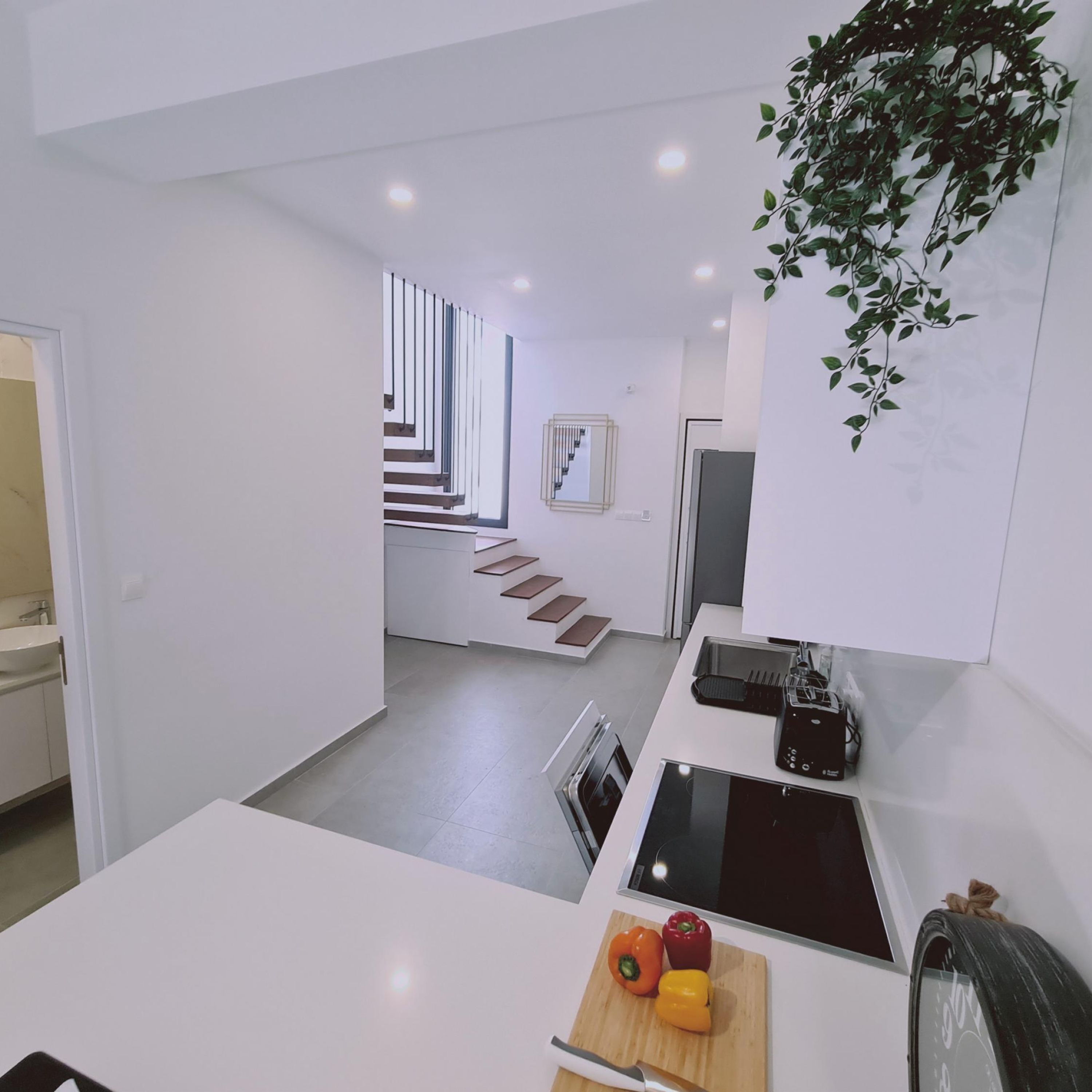 A modern kitchen with a white countertop, a stove, and a microwave. There is a staircase leading to another room.