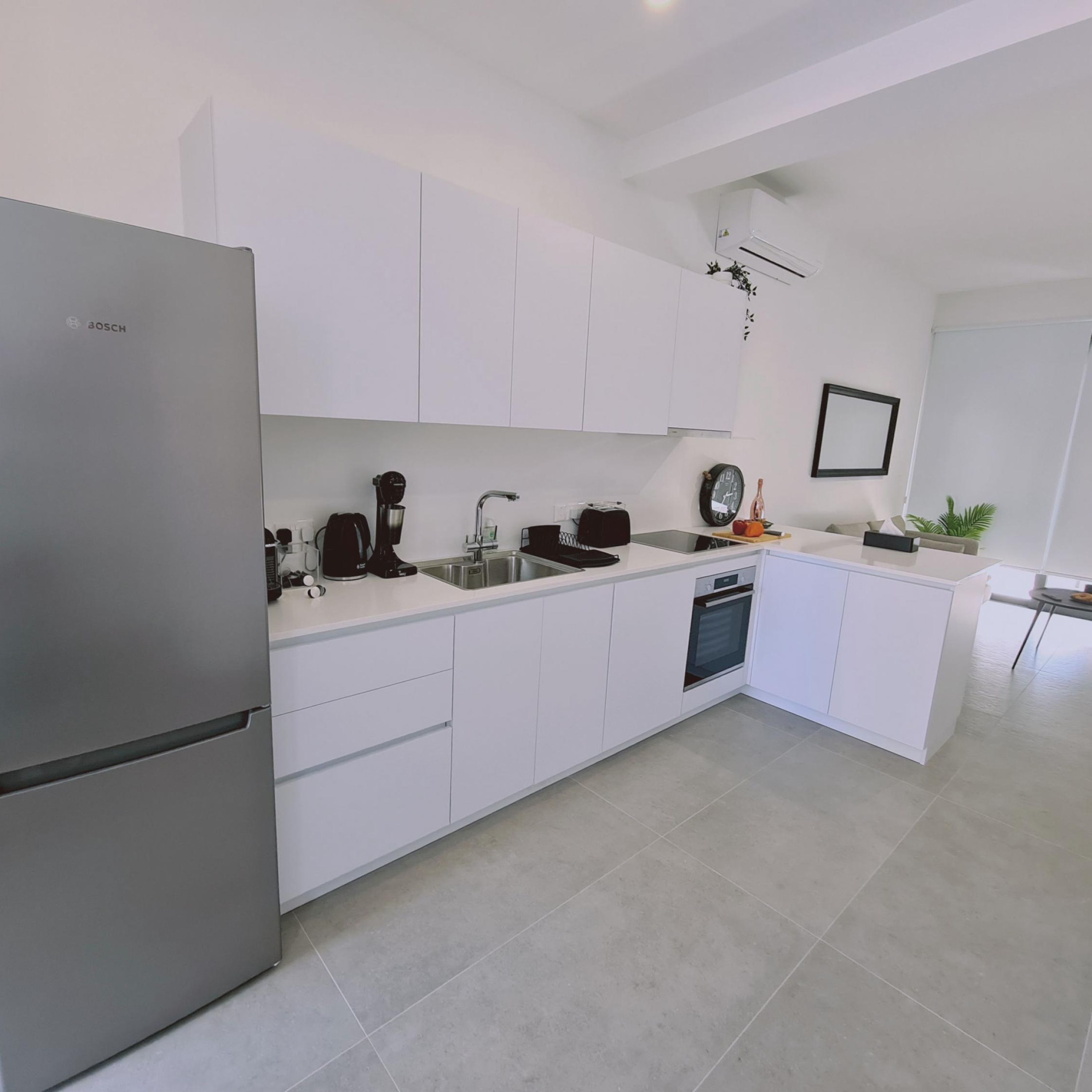 A modern kitchen with white cabinetry, a Bosch refrigerator, a coffee machine, and a dishwasher.
