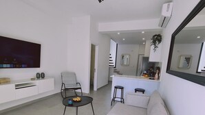 Ein modernes Wohnzimmer mit Flachbildfernseher, einer Couch, einem Essbereich und einer Küche im Hintergrund, sowie einem großen Spiegel.