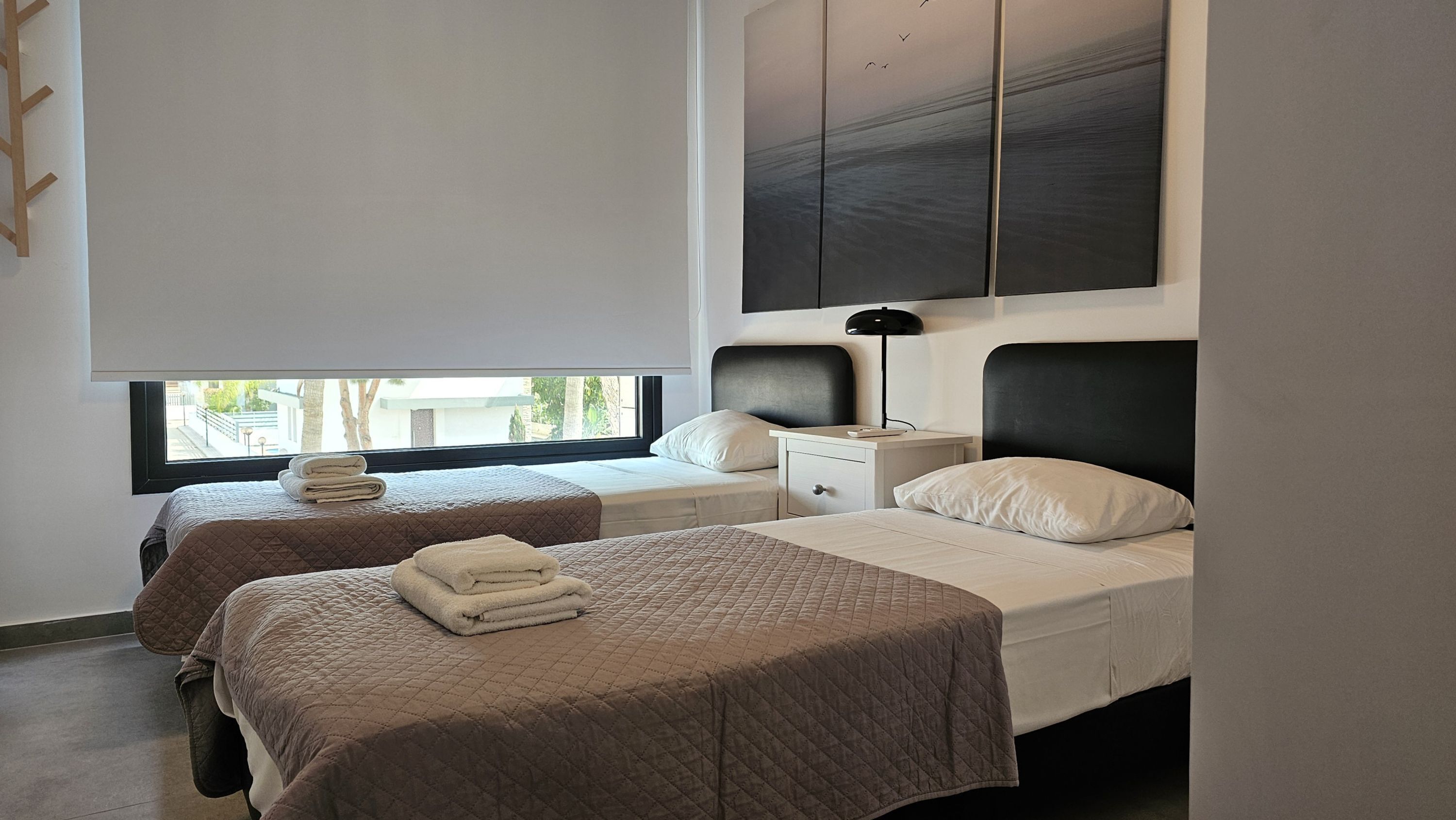 A modern hotel room with two beds, a large window, and a view of the outdoors.