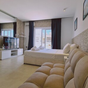 A modern hotel room with a bed, a sofa, a TV, and a view of the city. - 71 AN -stay Lavish Studio (Ayia Napa)