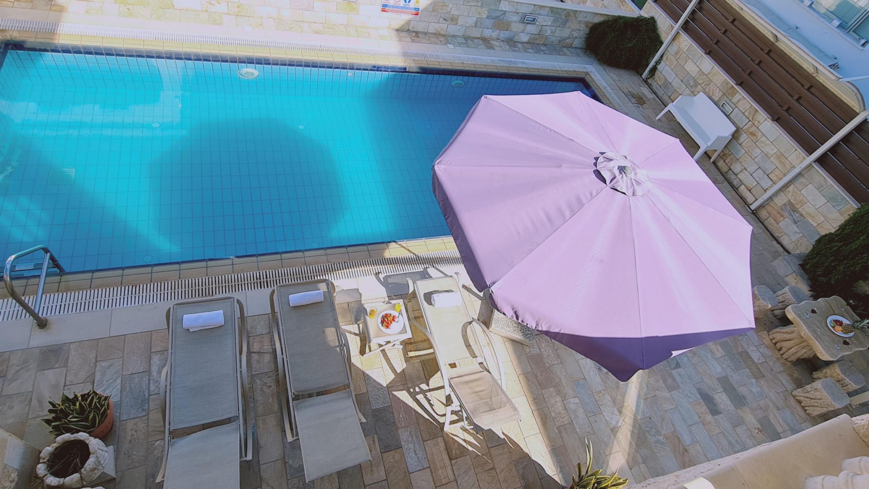 Uma piscina com bordas azulejadas, um guarda-sol roxo e cadeiras de descanso.