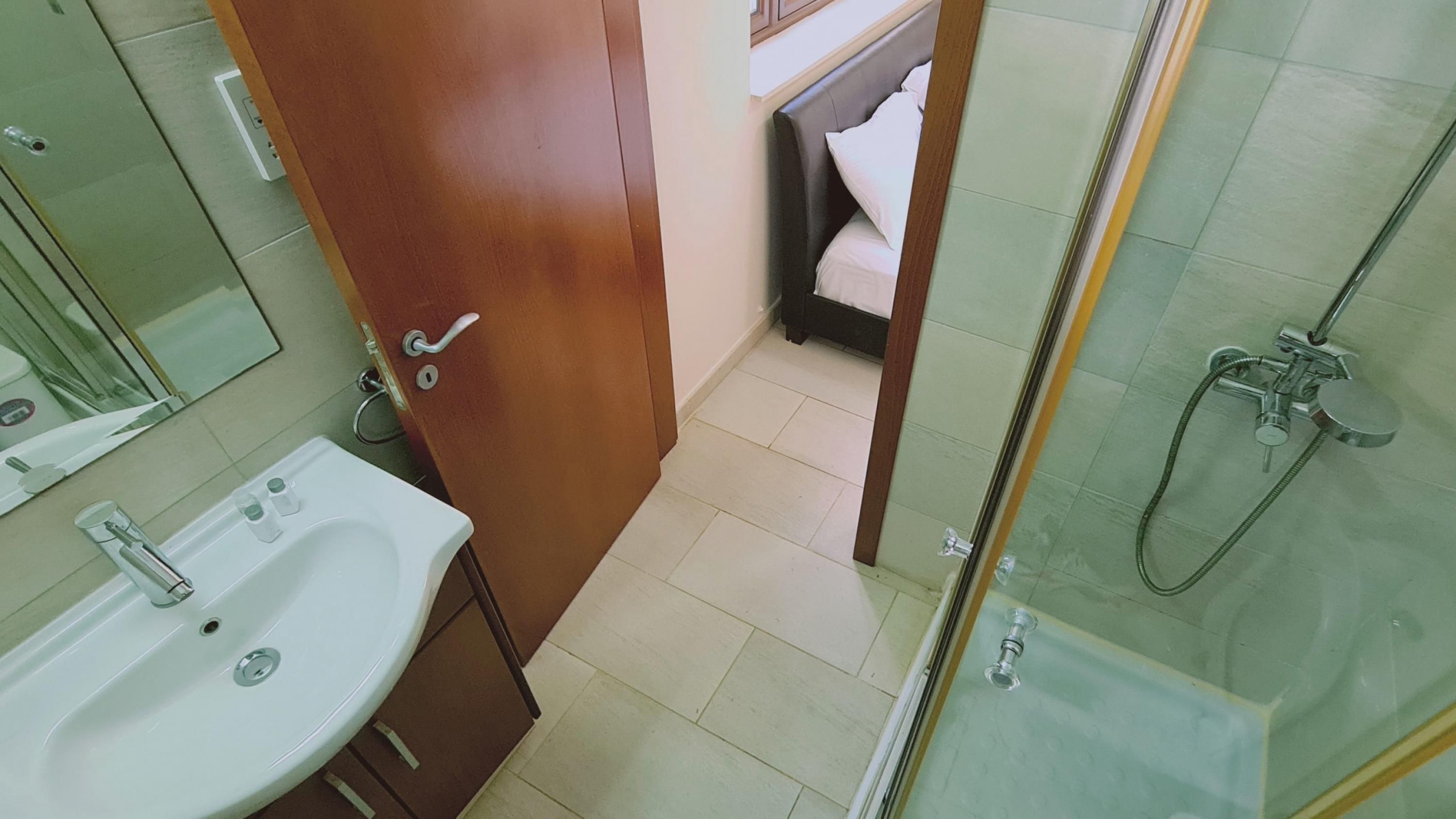 A bathroom with a sink, mirror, shower, and a door leading to a bedroom.
