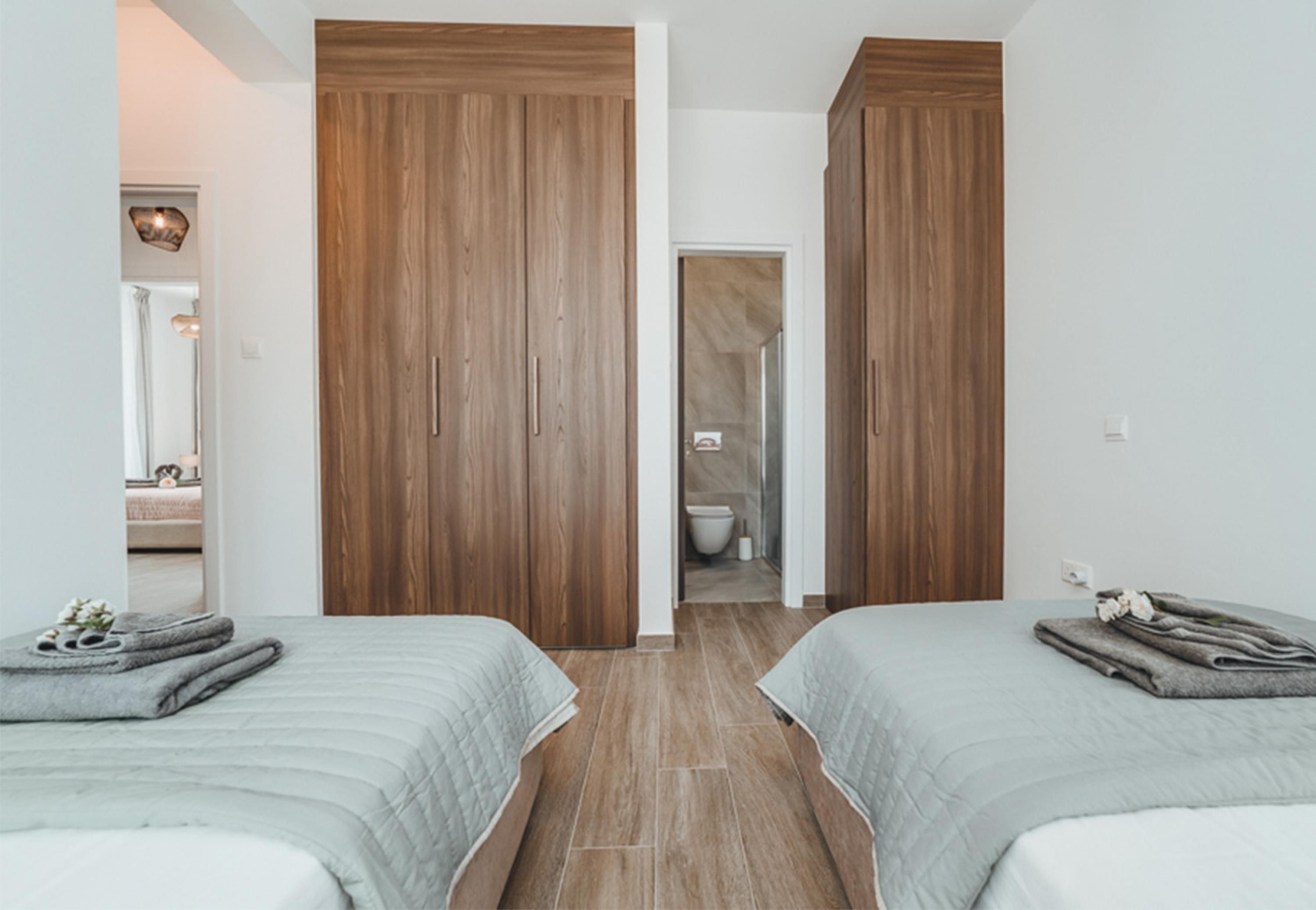 Een slaapkamer met twee bedden, houten kasten en een zichtbare badkamer door een open deur.
