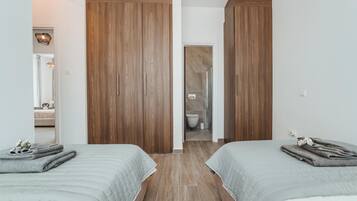 Een slaapkamer met twee bedden, houten kasten en een zichtbare badkamer door een open deur.