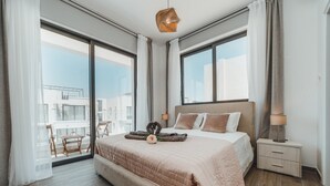 Una camera da letto moderna con un letto grande, un comodino e vista sulla città attraverso ampie finestre.