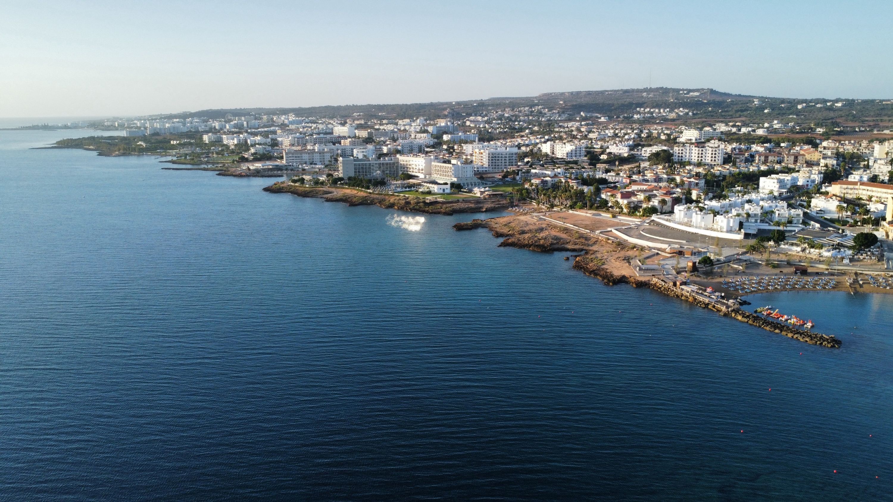 Vista aérea de una ciudad costera con un puerto deportivo, edificios y un cielo despejado.