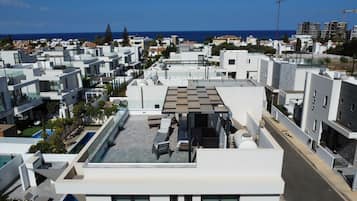 Um edifício residencial moderno com terraço no telhado, apresentando piscina, espreguiçadeiras e um pergolado.