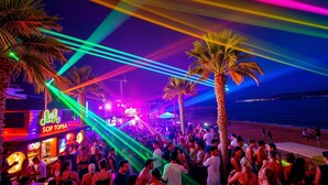 Eine belebte Bar am Strand, mit Palmen und bunten Lichtern.