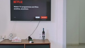 Televisão de tela plana na parede exibindo a tela de login do Netflix.