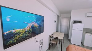 Une cuisine moderne équipée d’un four à micro-ondes, d’un réfrigérateur et d’un évier. Un téléviseur à écran plat fixé au mur diffuse une vue panoramique sur la côte.