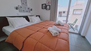 Ein Hotelzimmer mit einem großen Bett, weißer Bettwäsche, einer orangefarbenen Decke und Blick auf den Außenbalkon.