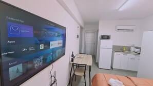A hotel room with a TV displaying various apps, a small dining table with chairs, a microwave, a refrigerator, and a sink in the kitchenette. - 100 AN - Napa Living 19 (Ayia Napa)