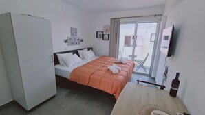 A hotel room with a bed, a TV, a table with a bottle, and a view of the outside. - 100 AN - Napa Living 19 (Ayia Napa)