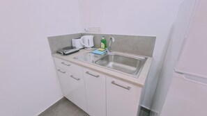 A compact kitchenette with a stainless steel sink, a kettle, a scale, and a bottle of dish soap. - 100 AN - Napa Living 18 (Ayia Napa)