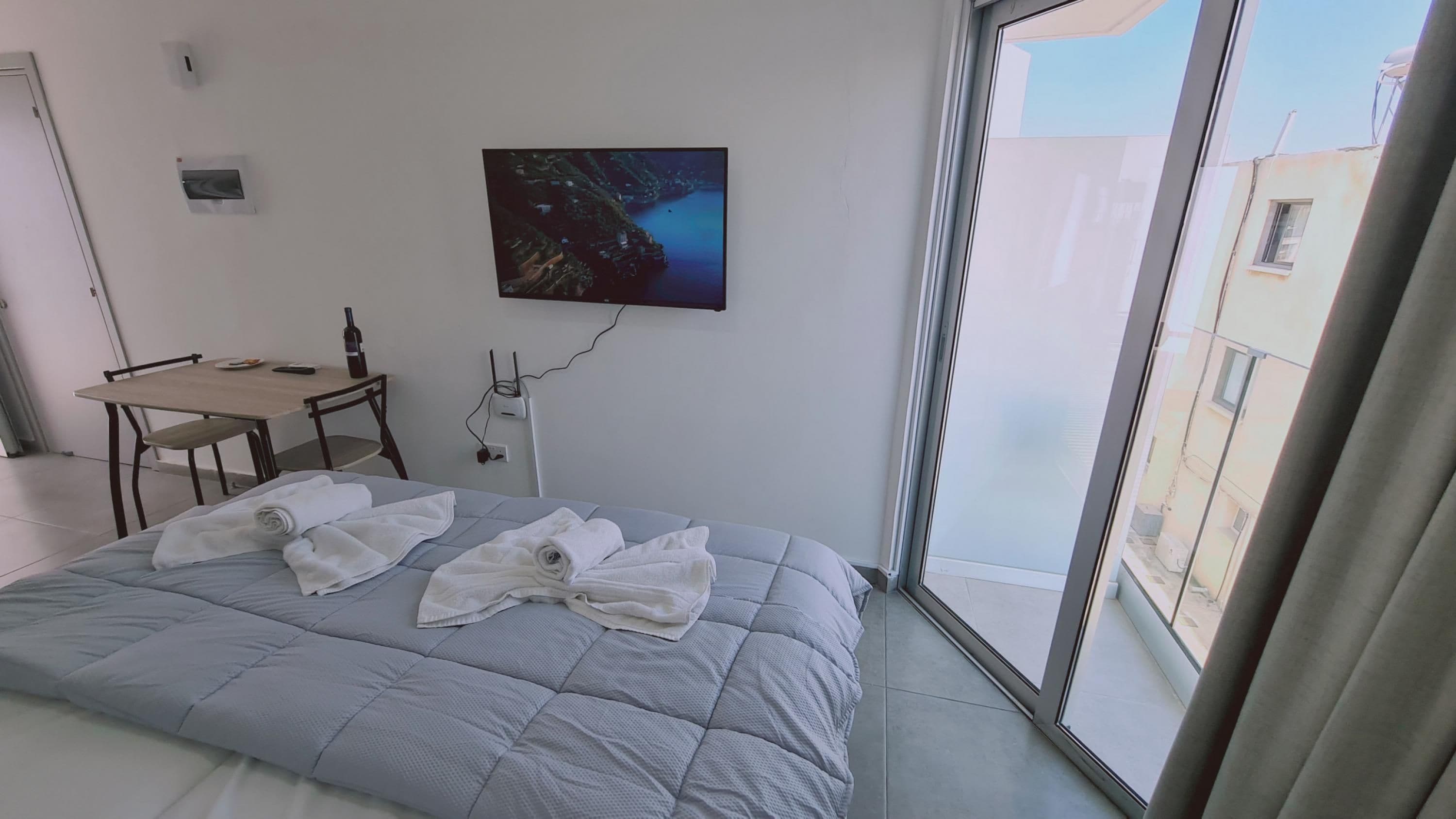 A hotel room with a bed, a desk, a chair, a painting, and a window.
