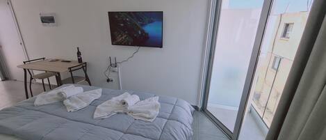 A hotel room with a bed, a desk, a chair, a painting, and a window.
