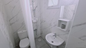 A bathroom with a toilet, shower, sink, and marble-tiled walls. - 100 AN - Napa Living 18 (Ayia Napa)