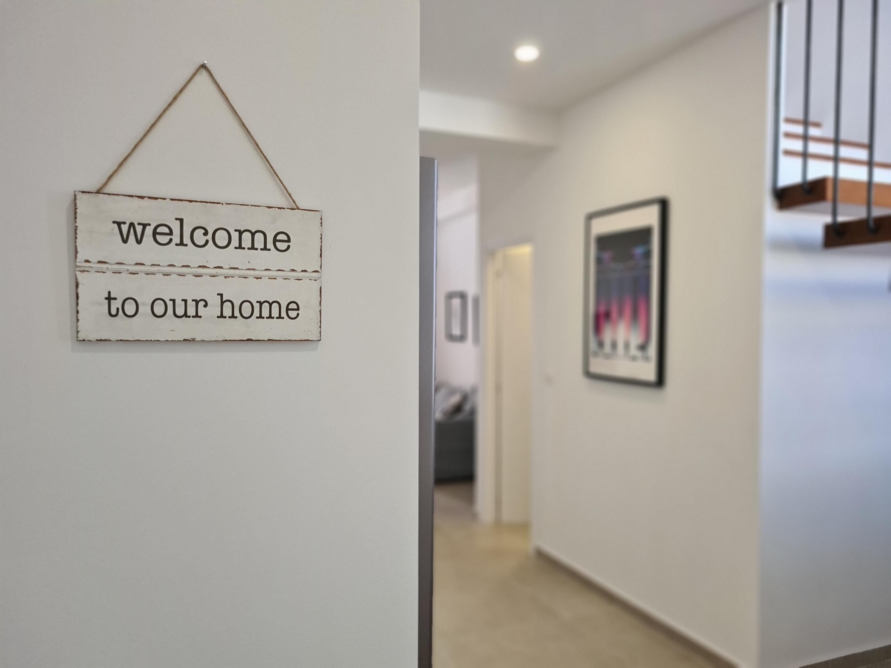 A hallway with a 'welcome to our home' sign and a framed picture on the wall.