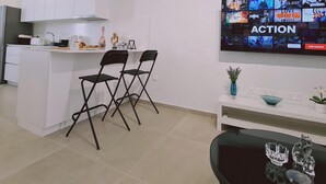 A modern kitchen with white cabinets, a central island with chairs, and a flat-screen TV displaying a Netflix interface. - 46 PRO - Stay Anemone 20 (Paralimni)