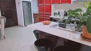Una cocina moderna con armarios rojos, una isla central con taburetes, un refrigerador y una cafetera.
