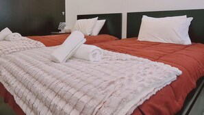 Habitación de hotel con dos camas, cada una con colcha roja y almohadas blancas. Un suave y esponjoso edredón blanco está en el suelo, y hay un equipo de aire acondicionado en la pared.