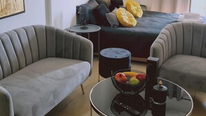 Ein modernes Schlafzimmer mit einem Bett, zwei Sesseln, einem runden Couchtisch mit Obst und einer Lampe, sowie einem Bild an der Wand.