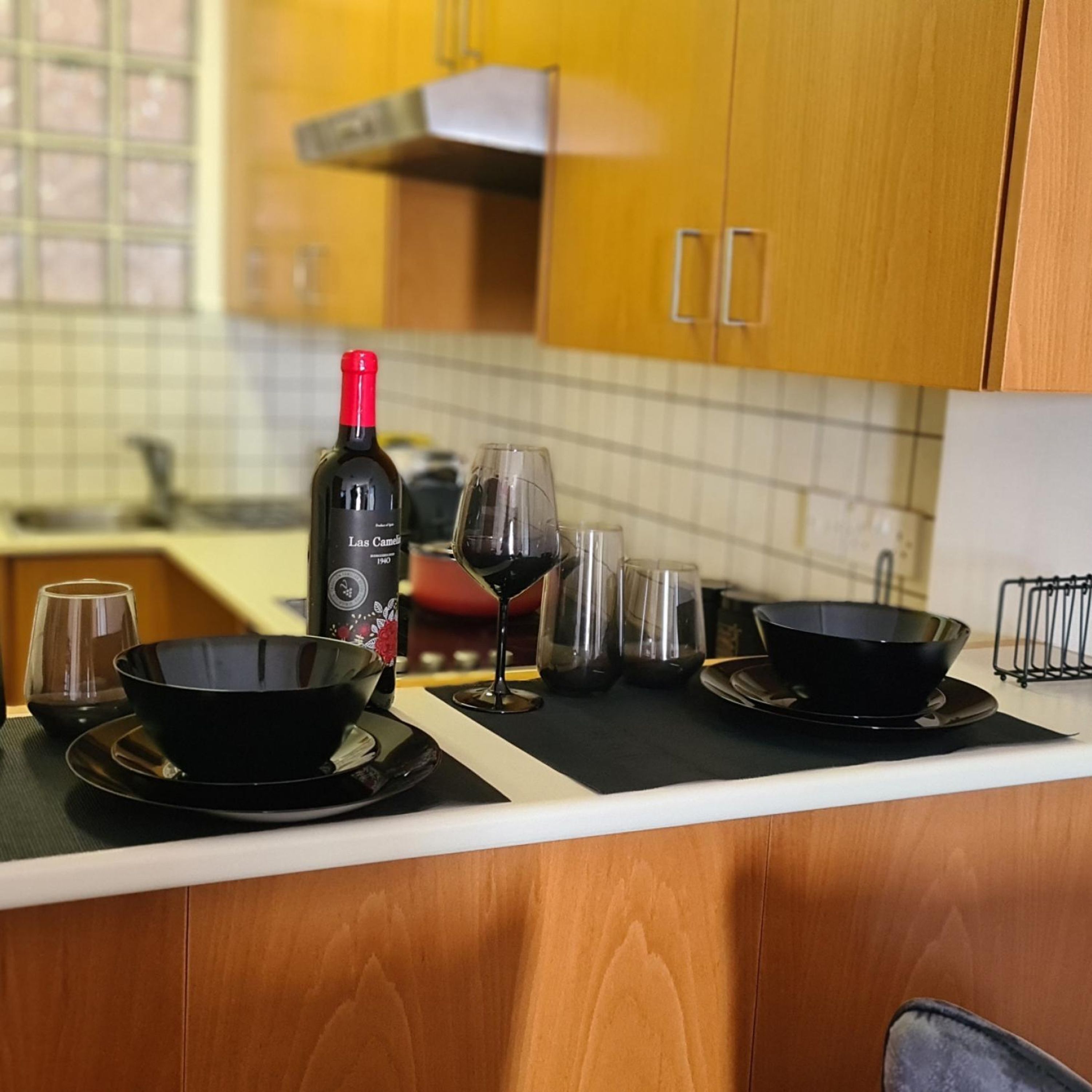 A kitchen counter with a bottle of wine, glasses, and a black bowl.