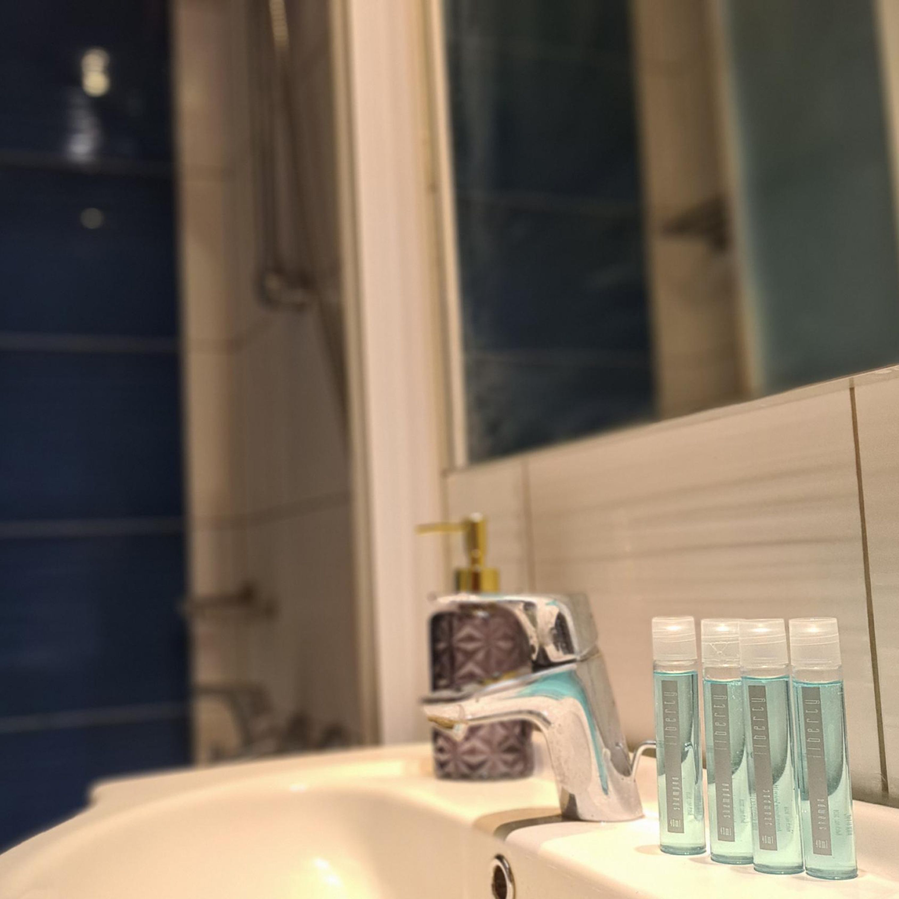 A bathroom sink with a mirror, a faucet, and four bottles of blue liquid soap.