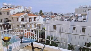 Ein Balkon mit Glastisch und Stühlen mit Blick auf ein Wohngebiet mit weißen Gebäuden und roten Ziegeldächern.