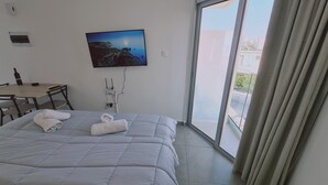 Habitación de hotel con cama, escritorio, televisor montado en la pared y vista a través de una puerta corrediza de vidrio.