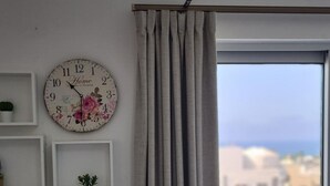 Une pièce avec une horloge, une fenêtre avec des rideaux et une vue sur des immeubles.