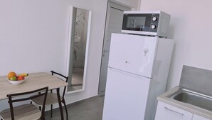 Une cuisine compacte avec un réfrigérateur blanc, un four à micro-ondes et un évier. On y trouve une table à manger avec des chaises et un saladier rempli de fruits.