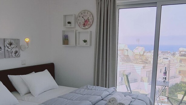 Une chambre avec un grand lit, une vue sur la ville depuis un balcon et une horloge au mur.