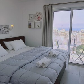 A bedroom with a large bed, a view of the city through a balcony, and a clock on the wall. - 100 AN - Napa Living 41 (Ayia Napa)