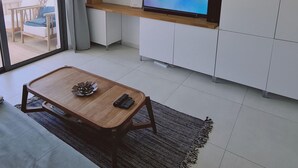 A modern living room with a TV on a wooden shelf, a dining table with chairs, and a sliding glass door leading to a balcony. - 78 LCA - Stay Kallucci s Maison de la mer (Larnaca)
