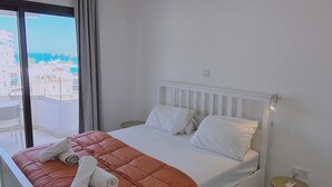 A modern hotel room with a large bed, a small bedside table, and a view of the city through the window. - 78 LCA - Stay Kallucci s Maison de la mer (Larnaca)