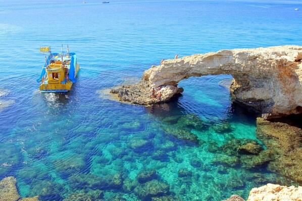 A clear blue sea with a boat named 'YELLOW SUBMARINE' and a natural rock arch formation. - 100 AN - Napa Living 36 (Ayia Napa)