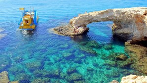 Mar azul cristalina con un barco llamado 'YELLOW SUBMARINE' y una formación rocosa natural en forma de arco.