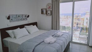Un dormitorio con cama, almohadas, vistas de la ciudad a través de un ventanal grande y un reloj en la pared.