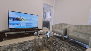 A living room with a flat-screen TV, a grey sofa, a glass coffee table, and a black entertainment unit. - 104 NIC - 403 Stay Cosmo City Suite (Nicosia)