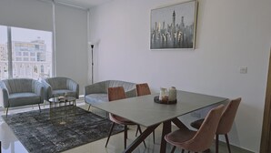 A modern dining area with a glass table, grey upholstered chairs, a black and grey rug, and a cityscape painting on the wall. - 104 NIC - 403 Stay Cosmo City Suite (Nicosia)