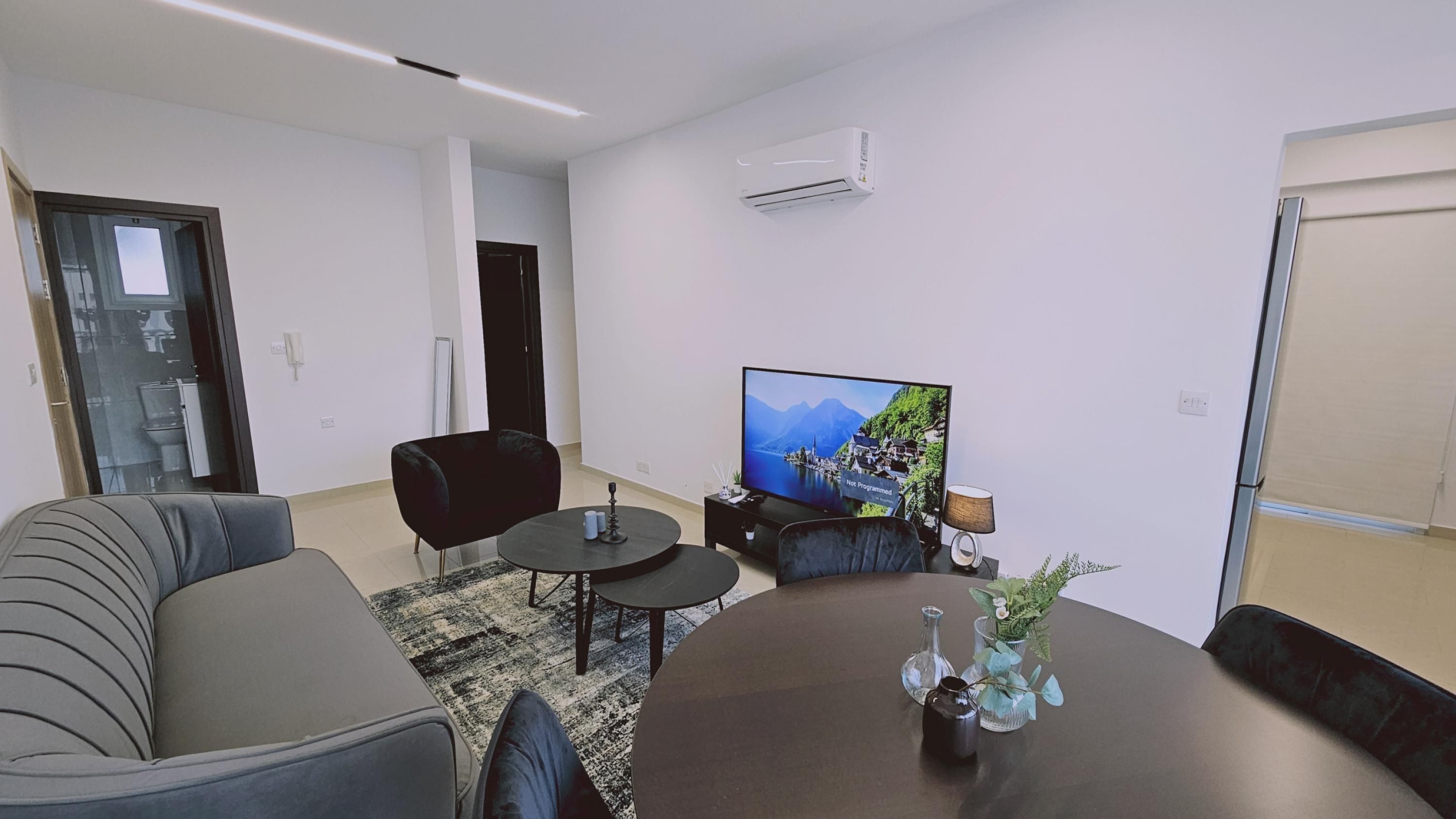 Ein modernes Wohnzimmer mit einer Couch, einem Couchtisch, einem Fernseher und einem kleinen Beistelltisch mit Dekoration.