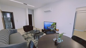 Un soggiorno moderno con un divano, un tavolino da caffè, una TV e un piccolo tavolino laterale con oggetti decorativi.