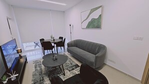 Un soggiorno moderno con un divano grigio, un tavolino rotondo e un tavolo da pranzo con sedie. Appeso al muro c'è un quadro e un televisore su un mobile.