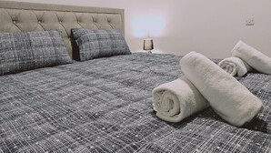 Camera da letto con un letto, cuscini, una lampada e asciugamani arrotolati.