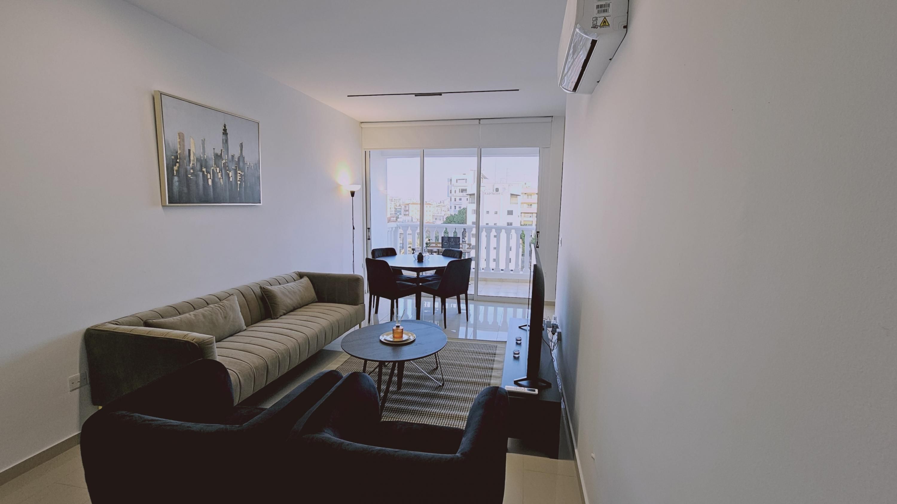 Un salon moderne avec un canapé, une table basse et une table à manger avec des chaises. Une grande fenêtre offre une vue sur la ville.