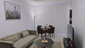 Un salon moderne avec un canapé, une table ronde entourée de chaises, un téléviseur et un tableau accroché au mur.