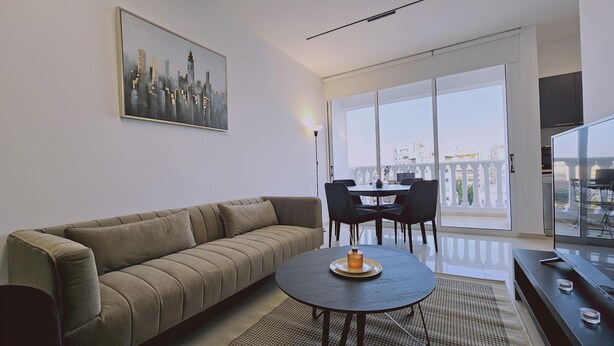 Un salon moderne avec un canapé, une table ronde agrémentée d’une bougie et un balcon offrant une vue sur la ville.