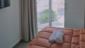 Ein Zimmer mit einem Bett, einem Fenster mit Vorhängen und Blick auf Gebäude.